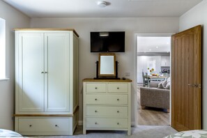 Ein Schlafzimmer mit Kleiderschrank, Schminktisch, Fernseher und einer offenen Tür zu einem Wohnbereich.