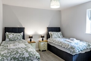 Ein Doppelzimmer mit zwei Einzelbetten, Nachttischen, Lampen und einem Fenster.