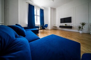 A modern living room with a large sofa set, a flat-screen TV mounted on the wall, and a small table with decorative items. - Where the Danube Meets Downtown: Exclusive Scenic Suite – 536 (Budapest)