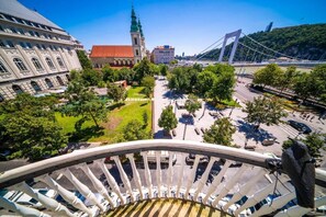 A view from a balcony overlooking a cityscape with a prominent bridge, a church, and a large building with a red roof. - Where the Danube Meets Downtown: Exclusive Scenic Suite – 536 (Budapest)