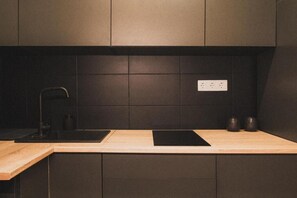 A modern kitchen with dark cabinetry, a wooden countertop, and a black induction cooktop. - Where the Danube Meets Downtown: Exclusive Scenic Suite – 536 (Budapest)