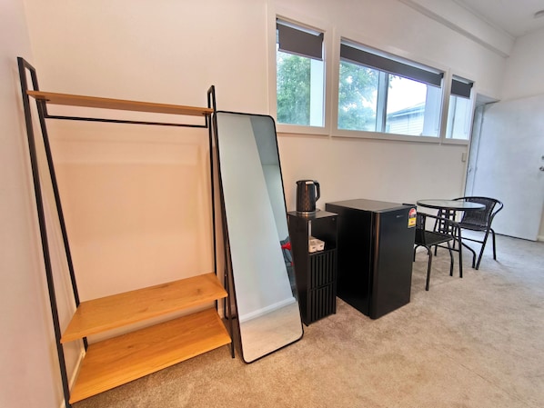 A room with a bed, a desk, a chair, a coffee maker, and a window.
