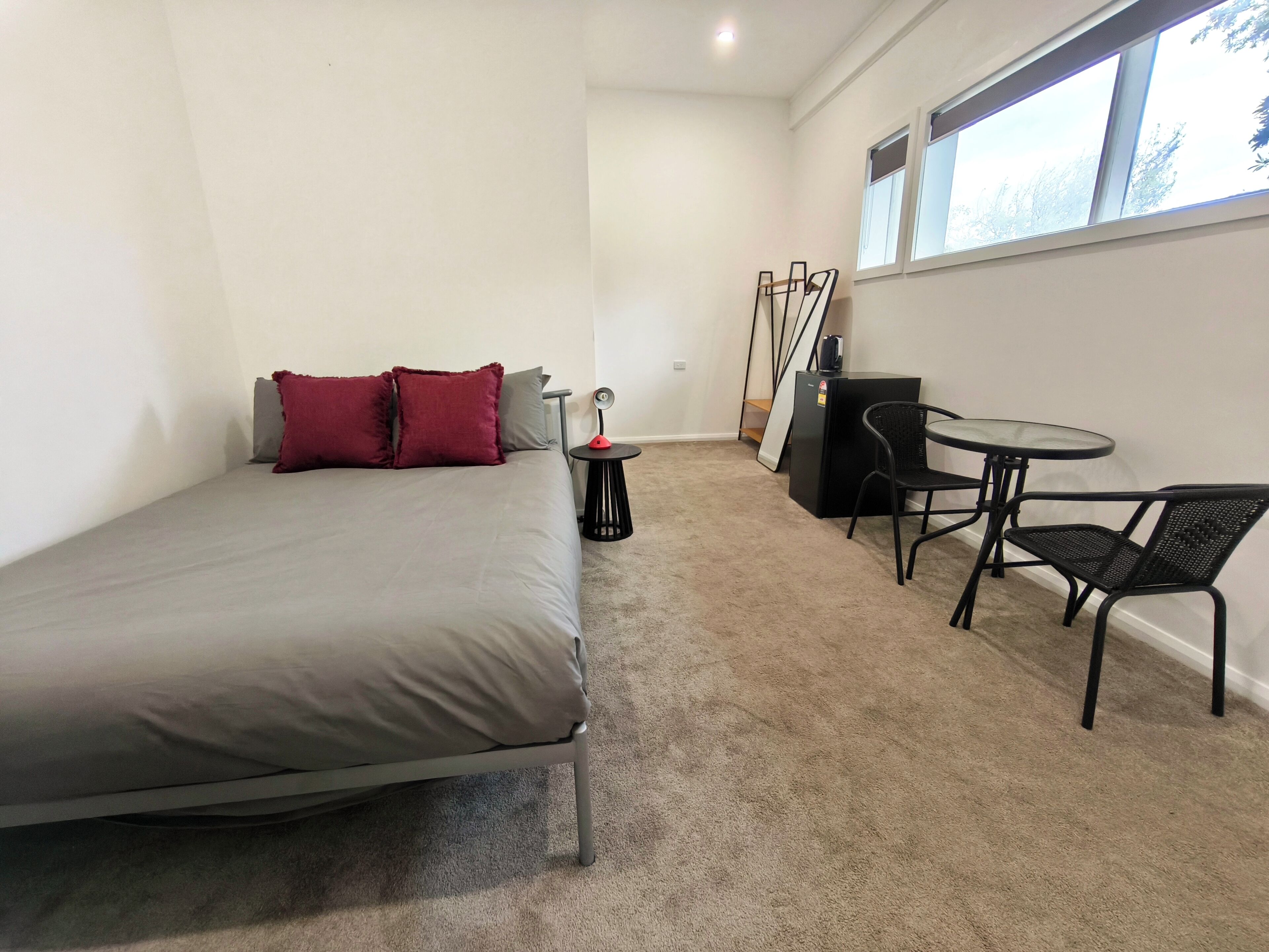 A bedroom with a bed, a desk with a chair, a small table, and a window.