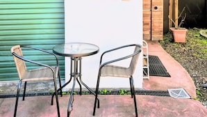 Un patio con una mesa y dos sillas, una puerta de garaje verde, y un muro con letrero 'UNIT B'.