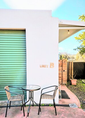 A patio area with a table and two chairs, a green garage door, and a wall with 'UNIT B' signage.