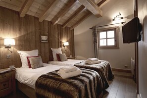 Ein Zimmer mit Holzwänden, zwei Betten mit weißer Bettwäsche, einem Fernseher und einem Fenster mit Vorhängen.