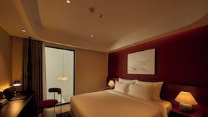 Quarto de hotel com cama, escrivaninha, cadeira e um quadro na parede.