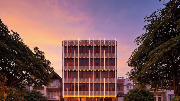 Um edifício moderno com fachada vertical, entrada destacada e faixa de pedestres na frente.