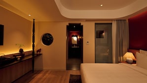 Quarto de hotel moderno com uma cama grande, uma escrivaninha e um banheiro visível através de uma porta aberta.
