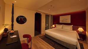 Quarto de hotel com cama, escrivaninha, cadeira e obra de arte na parede.
