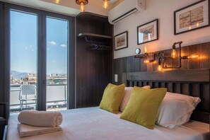 A hotel room with a bed, a view of the city, and a wall-mounted light fixture. - Captain Stam Suites Athens - CityStudio (Athina)