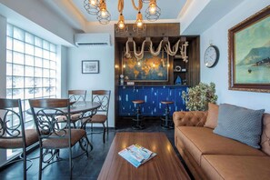 Ein Essbereich mit rundem Tisch und Stühlen, eine Bar mit Hockern, eine Couch und ein großes Fenster mit Blick.