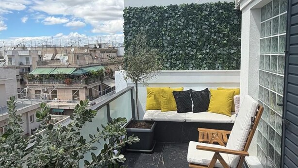 A balcony with a seating area, a potted plant, and a view of the cityscape. - Captain Stam Suites Athens - FamilyApartment (Athina)