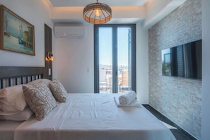 Ein Hotelzimmer mit Bett, einem Gemälde, einem Fernseher und Blick auf die Stadt durch große Fenster.