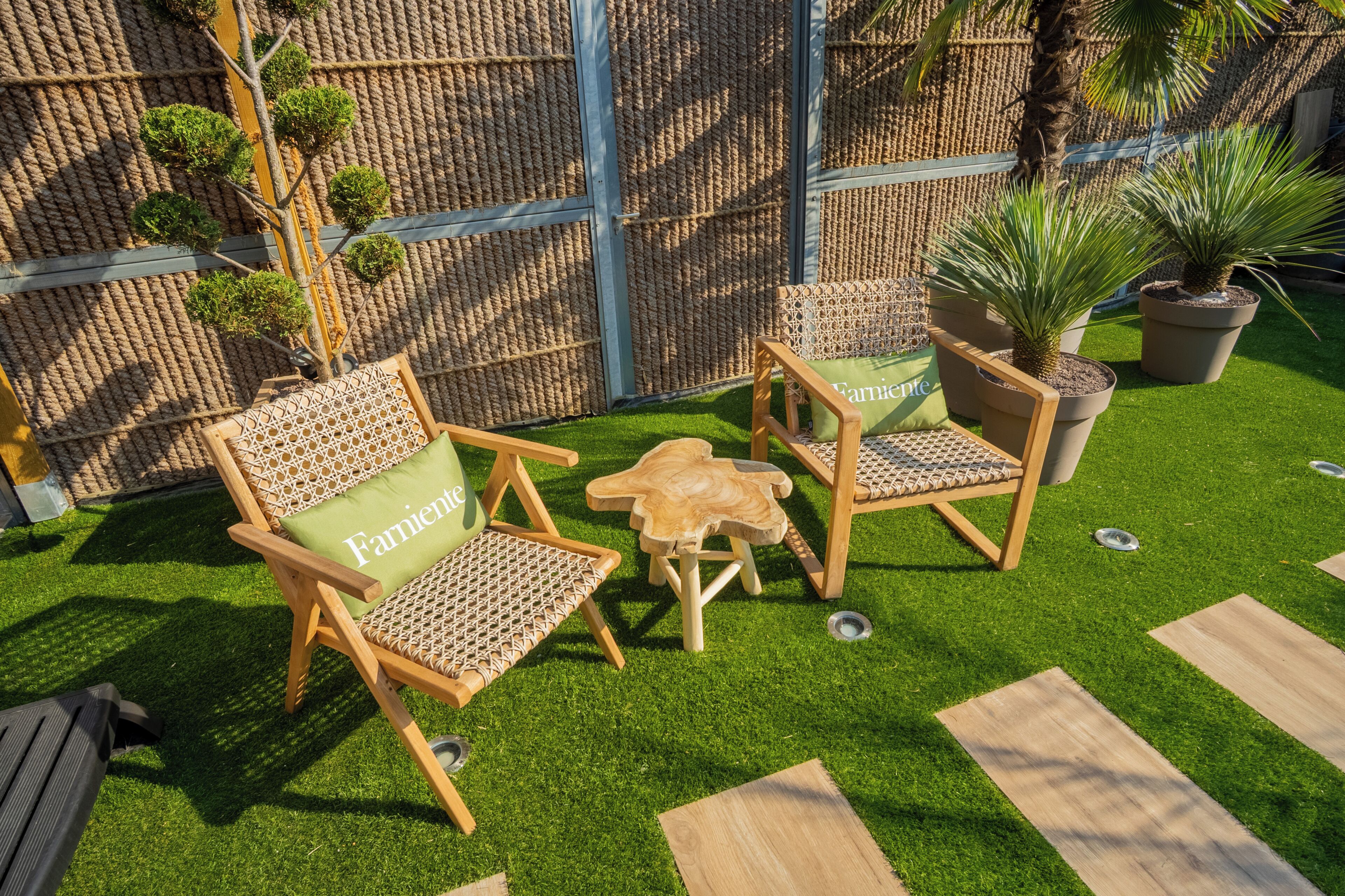 Een terras met twee houten stoelen en een kleine tafel, omringd door kunstgras en een sierhek.