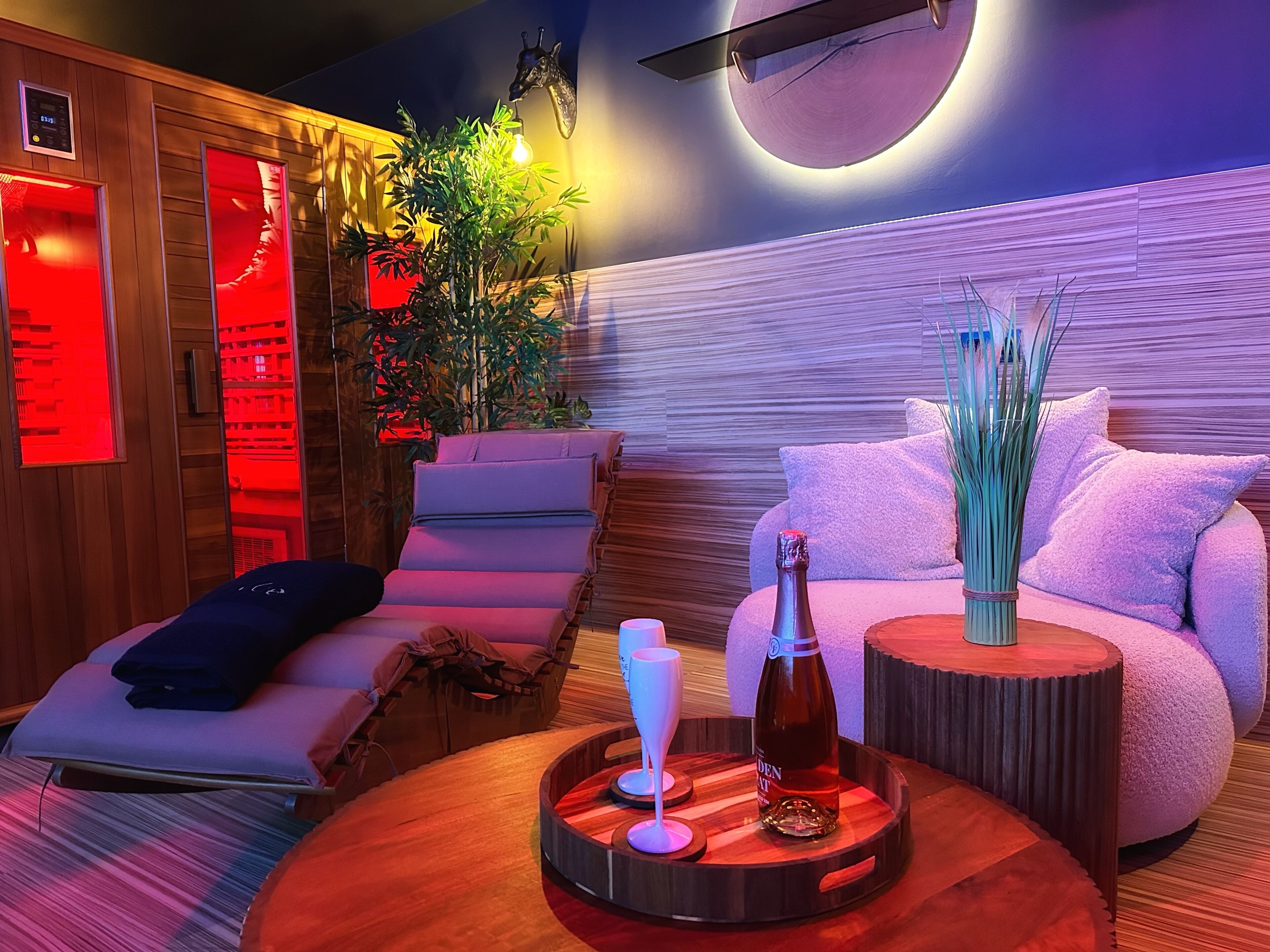 Une salle de spa équipée d’un fauteuil de massage, d’une table ronde en bois avec une bouteille et des verres, et d’un radiateur fixé au mur.