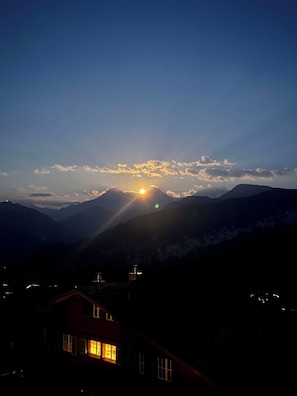 Eine Berglandschaft im Abendlicht mit einem Haus im Vordergrund.