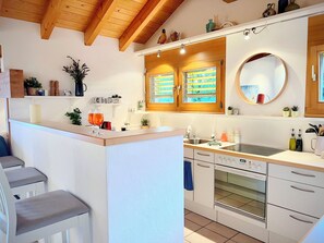 A modern kitchen with a central island, wooden ceiling beams, and a large round mirror above the sink. - Möösli Vue Appartement/Fewo Appartement/Fewo by Interhome (Beatenberg)