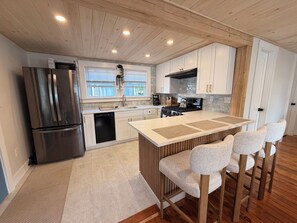 A modern kitchen with a stainless steel refrigerator, a dishwasher, a stove, and a sink. There are white cabinets and a wooden ceiling.
