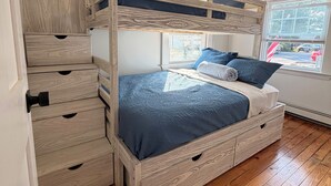En køjeseng med opbevaringsskuffer, et vindue med rullegardiner og en loftlampe.