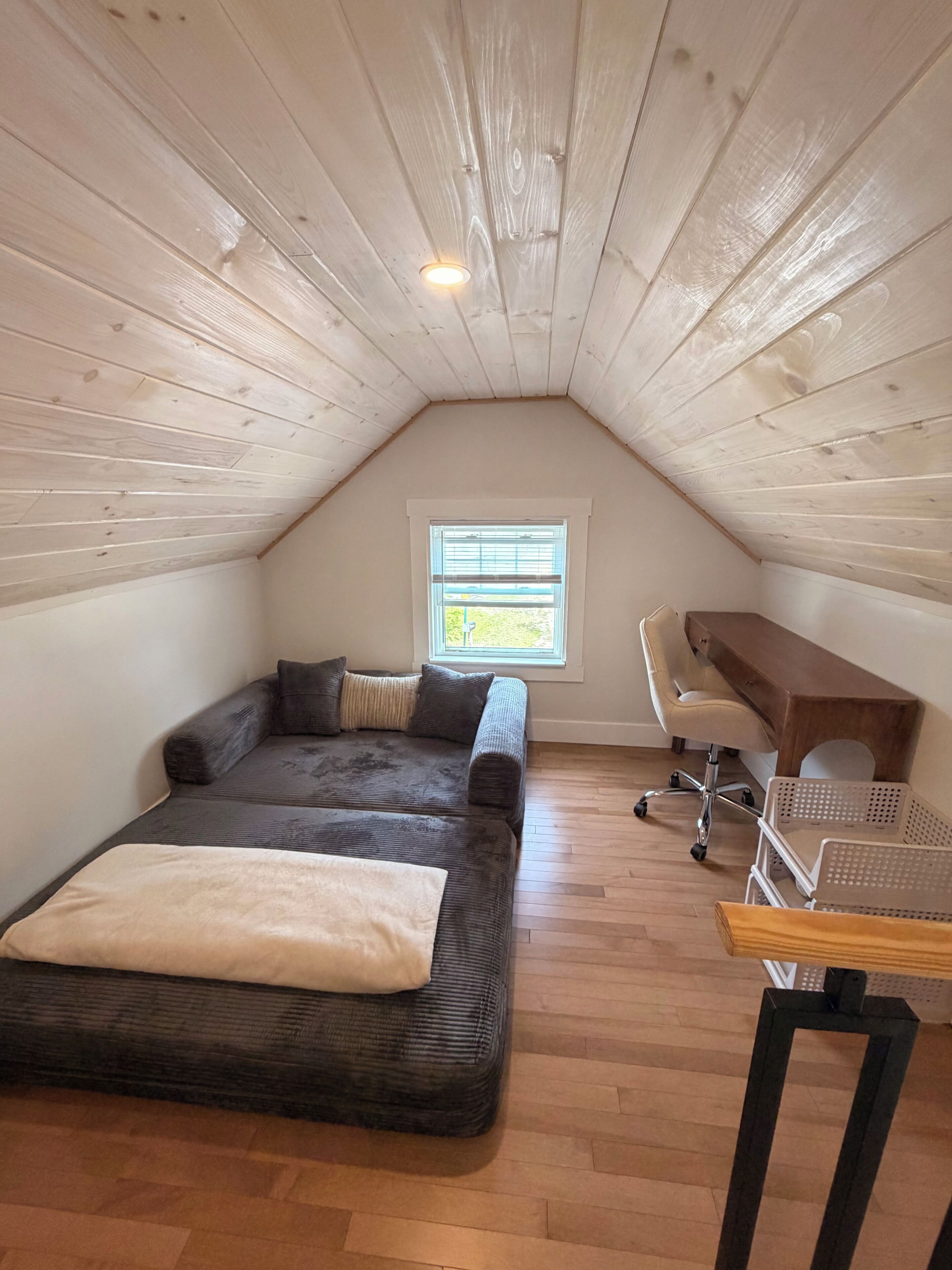 Une chambre aménagée en mezzanine, avec un plafond en pente, un lit, un bureau et une fenêtre.