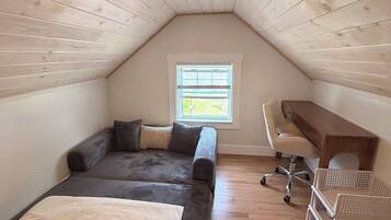 Une chambre aménagée en mezzanine, avec un plafond en pente, un lit, un bureau et une fenêtre.