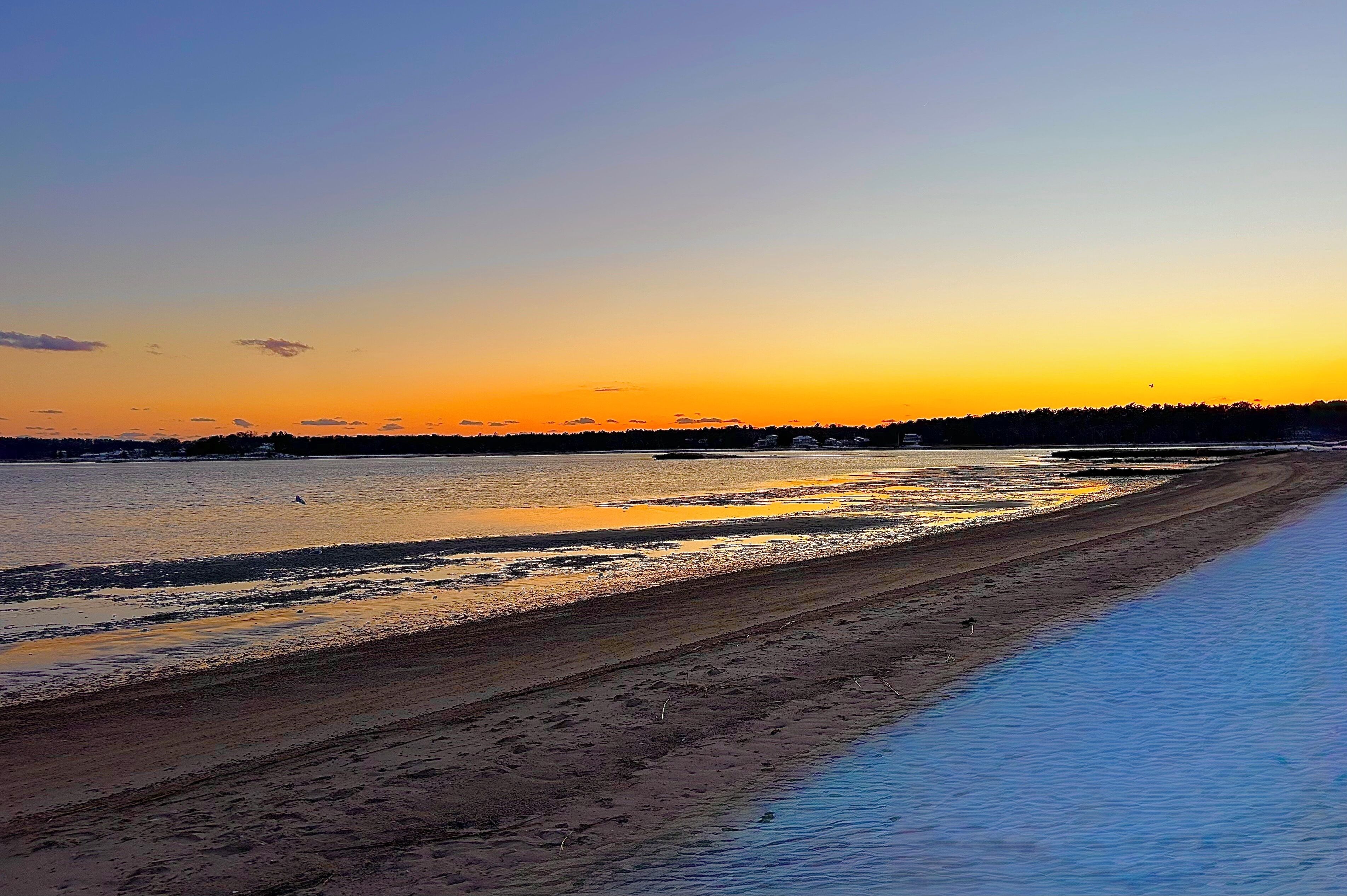 Une plage avec un ciel dégagé et une eau calme qui reflète le coucher de soleil.