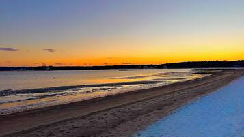 Une plage avec un ciel dégagé et une eau calme qui reflète le coucher de soleil.