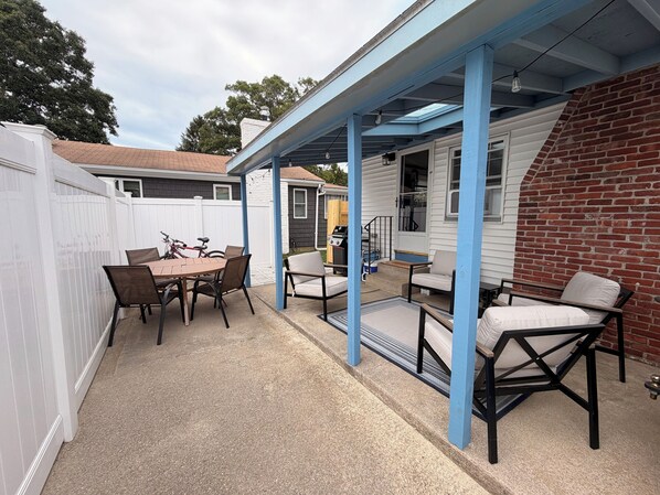 A covered patio area with a table and chairs, a grill, and a brick wall.