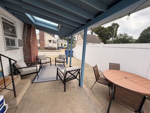 A covered patio area with outdoor furniture, a table, and a view of neighboring houses. - 3-bedroom cottage in Swifts Beach, relaxing coastal living, outdoor shower, AC. (Wareham)