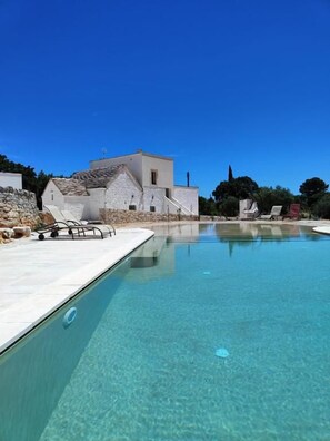 Una piscina cristalina con un muro de piedra y un edificio al fondo.