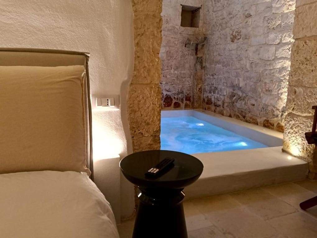 A room with a stone wall, a bathtub, and a remote control on a table.