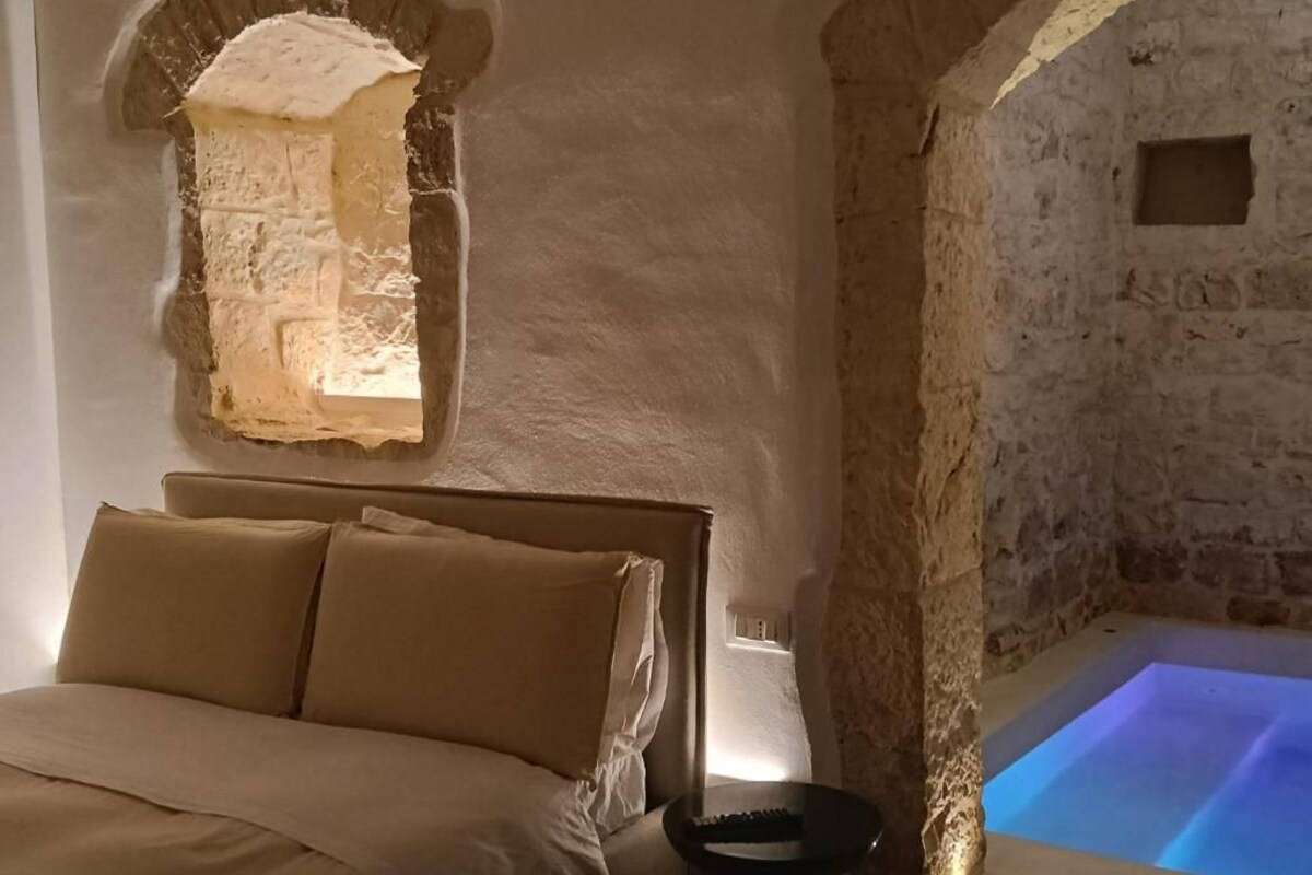 A bedroom with a bed, a nightstand, a stone wall, and a lit blue pool.