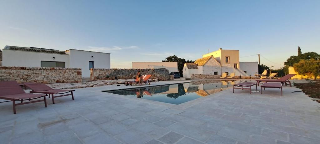 A pool area with lounge chairs, a stone wall, and modern buildings in the background.