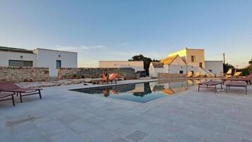 A pool area with lounge chairs, a stone wall, and modern buildings in the background.