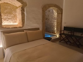 A bedroom with a bed, a stone wall, and a small pool.