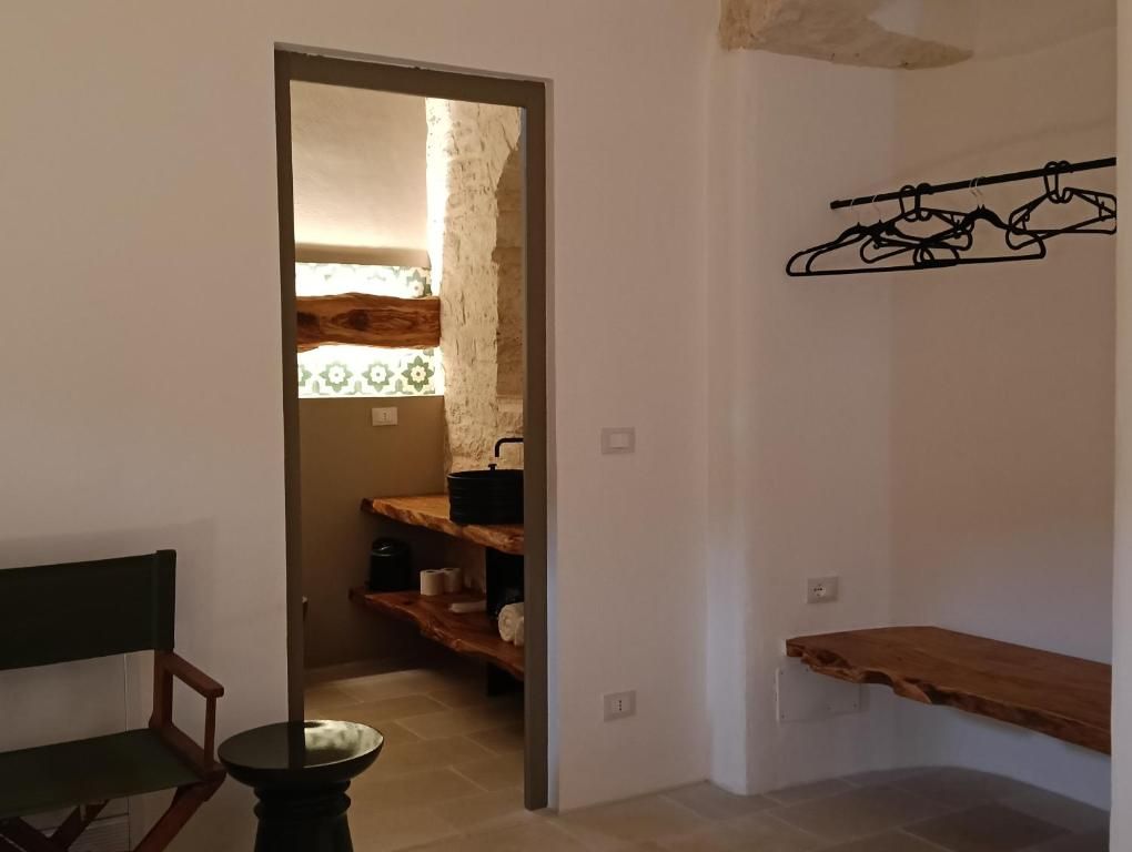 Un couloir avec un banc, une porte donnant sur une pièce dont un mur est décoré de motifs, et une étagère en bois sur laquelle sont suspendus divers objets.
