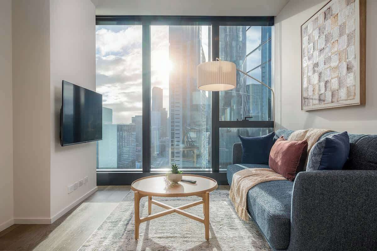 A modern living room with a large window, a flat-screen TV, a round coffee table, and a sofa.