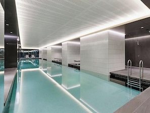 Ein modernes Hallenbad mit klarem Wasser, gefliesten Wänden und einer Decke mit Rasteroptik.