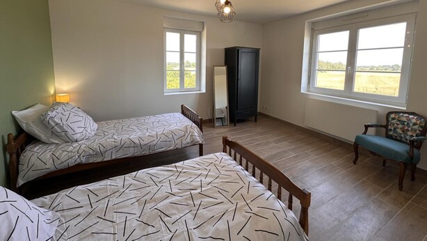 A bedroom with two beds, a cabinet, a chair, and a view of the outdoors.