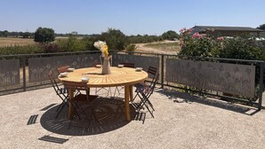 An outdoor patio with a round wooden table, chairs, and a vase of flowers.