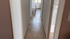 A narrow hallway with tiled flooring leading to a bedroom with a bed and a window.