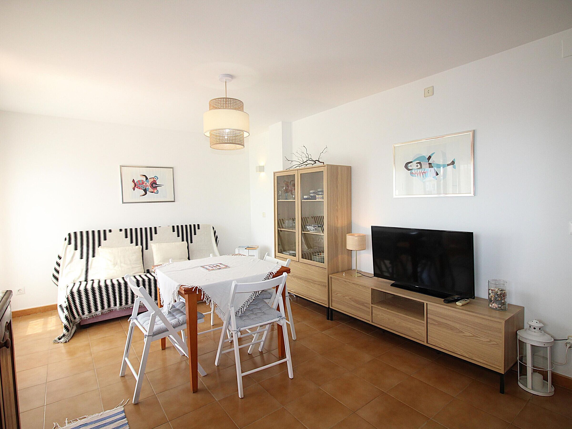 A living room with a dining table, chairs, a sofa, a TV, a cabinet, and artwork on the walls.