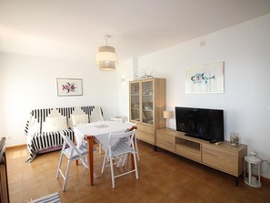 A living room with a dining table, chairs, a sofa, a TV, a cabinet, and artwork on the walls. - Bright apartment by the beach - 4 guests (Llançà)