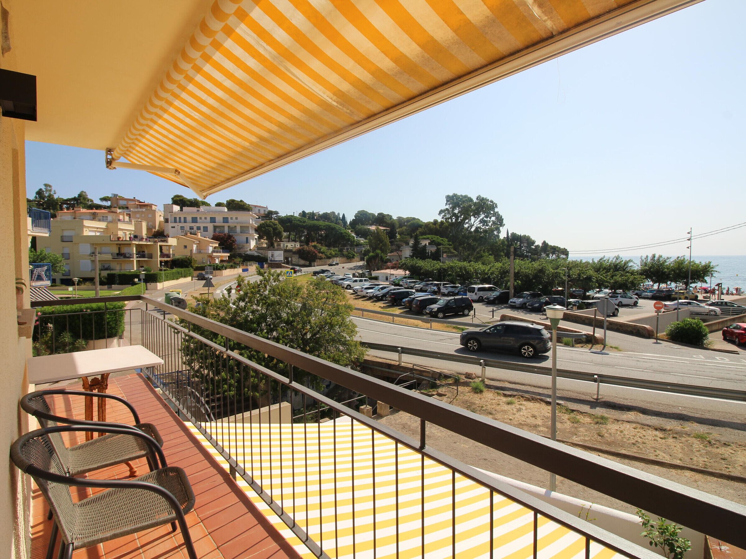 A balcony with a striped awning overlooking a parking area and a road with buildings in the background.