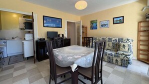 Ett kompakt bostadsutrymme med ett matbord, stolar, en soffa, en tv och ett litet kök.