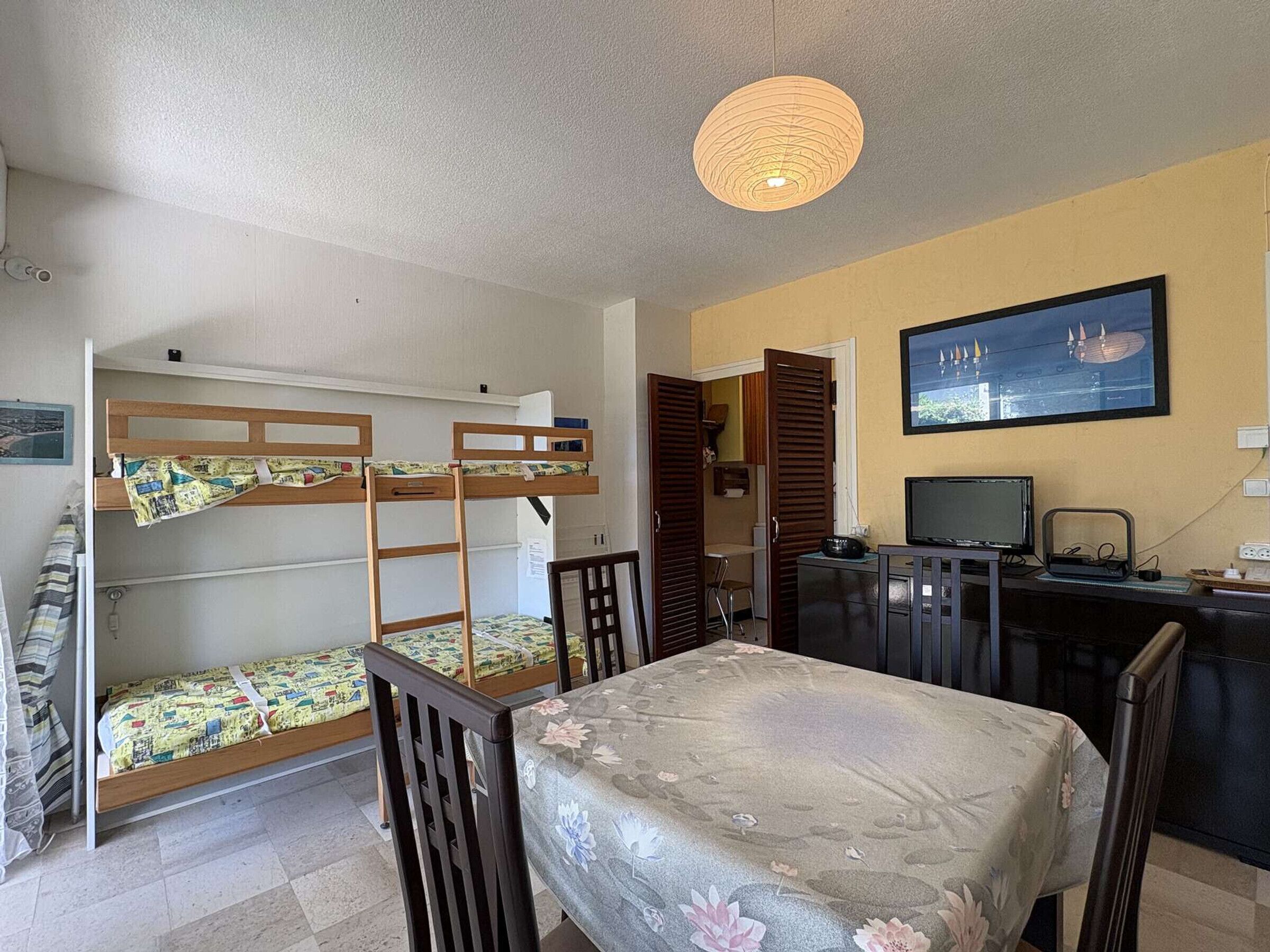 A room with bunk beds, a desk with a computer, a chair, and a bed with a floral bedspread.