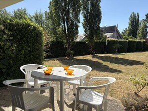 An outdoor patio with a round table and four chairs, surrounded by a well-maintained hedge and a lawn.