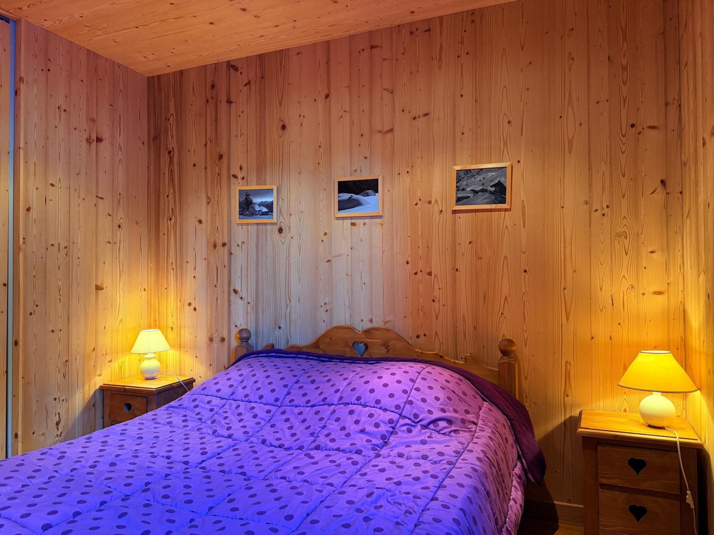 Een kamer met houten lambrisering, een bed, twee bedlampen en drie ingelijste foto's aan de muur.