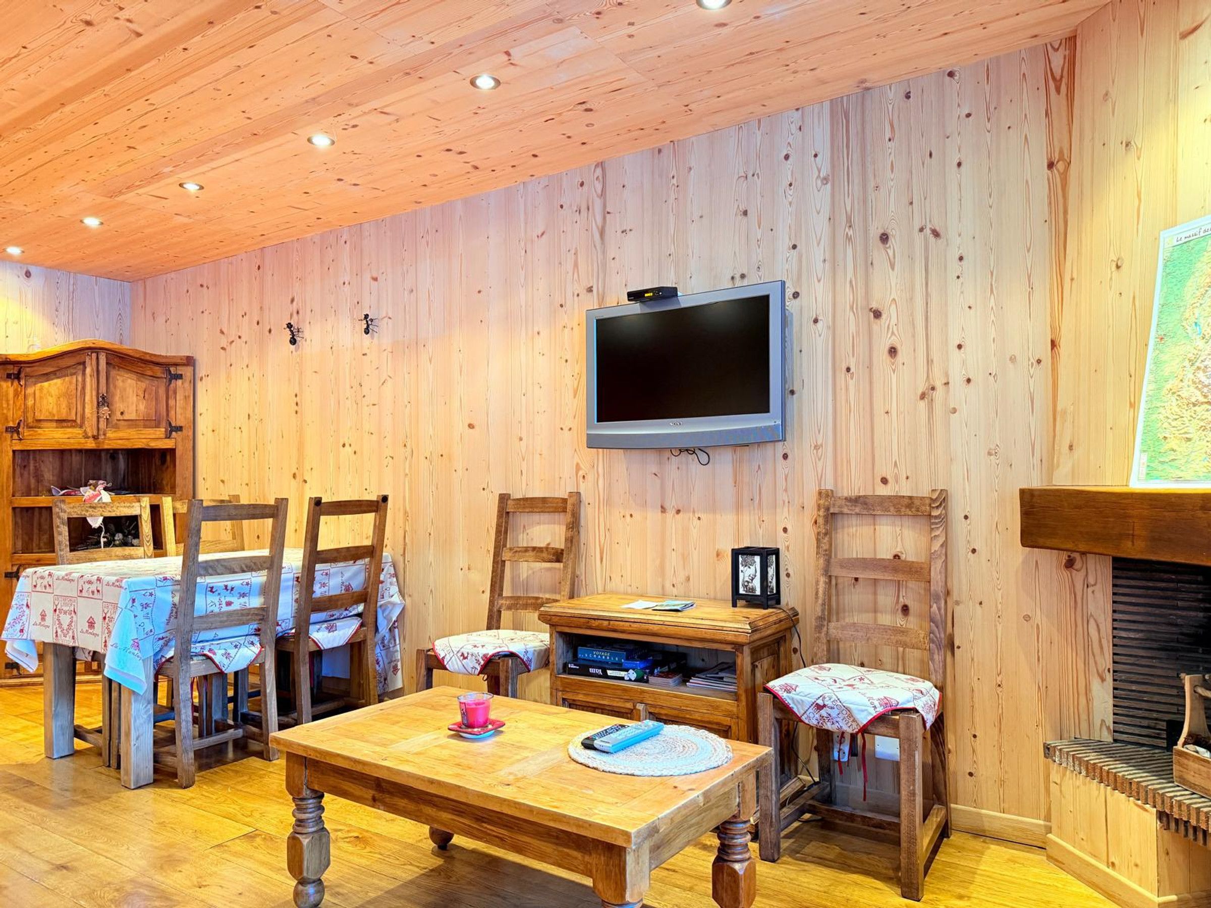 A wooden interior with a television mounted on the wall, a fireplace, and a dining area with wooden furniture.